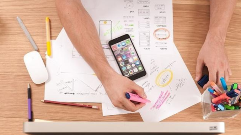 A birds-eye view of a hand at work on a desk covered in papers.