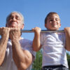 An image of an elderly man and a child doing chin ups.