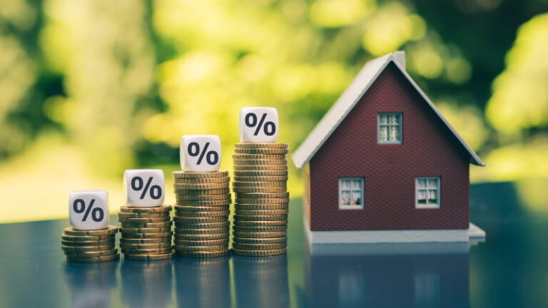 Image of a house next to stacks of coins with a percentage sign on top of them