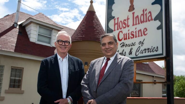 Restaurant owner and man pose in front of Indian restaurant
