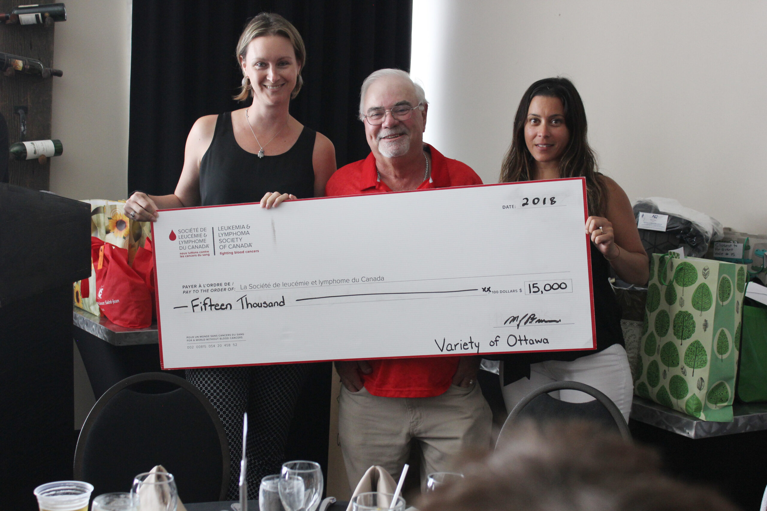 Three people stand holding an oversized cheque