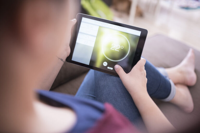 A woman holding a tablet with a smart home software open on it.