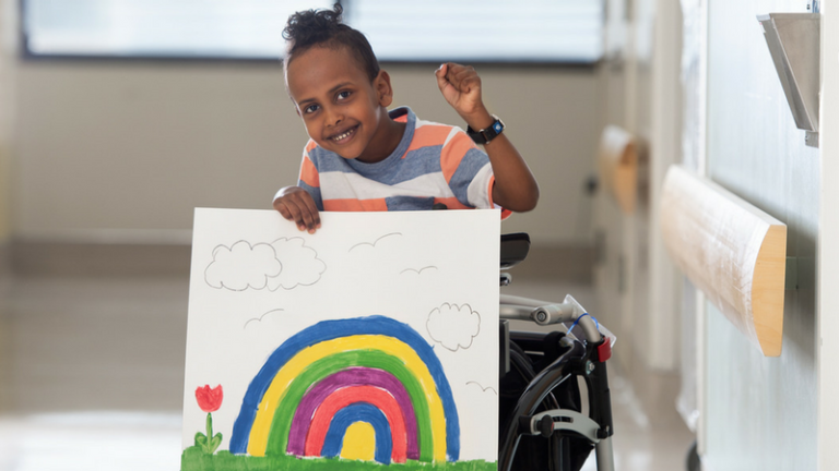 A boy using a mobility device stands smiling