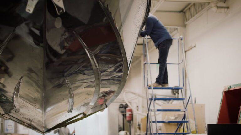A man on a ladder looks into a boat.