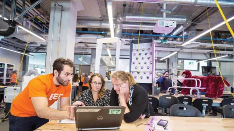 Three colleagues gather around a laptop to discuss a project