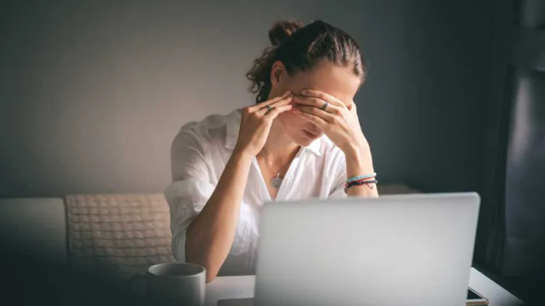 A woman sitting in front of a laptop at work rests her head on her hand