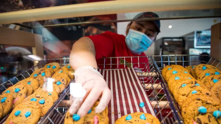 A man working at Tim Hortons takes a smile cookie off the rack.