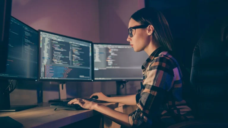 A woman looks intently at three monitors displaying complex data