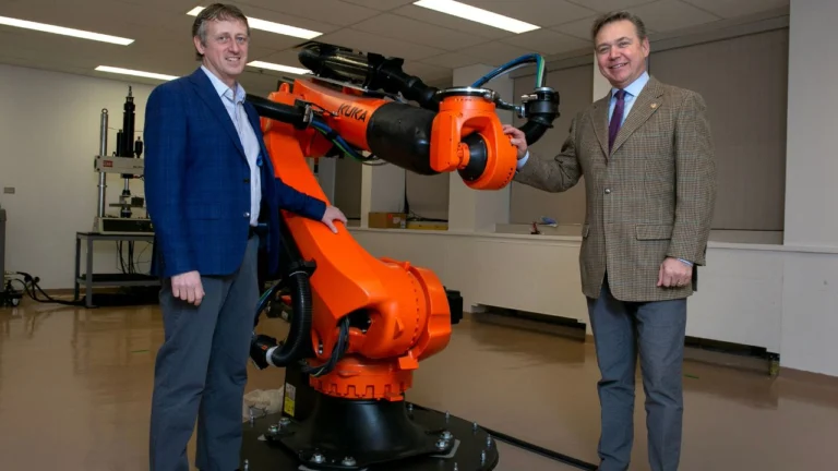 Portrait of two men standing next to an orange robotic arm