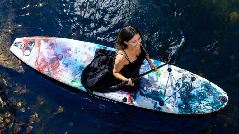 a woman kneels on a colourful paddleboard in the water