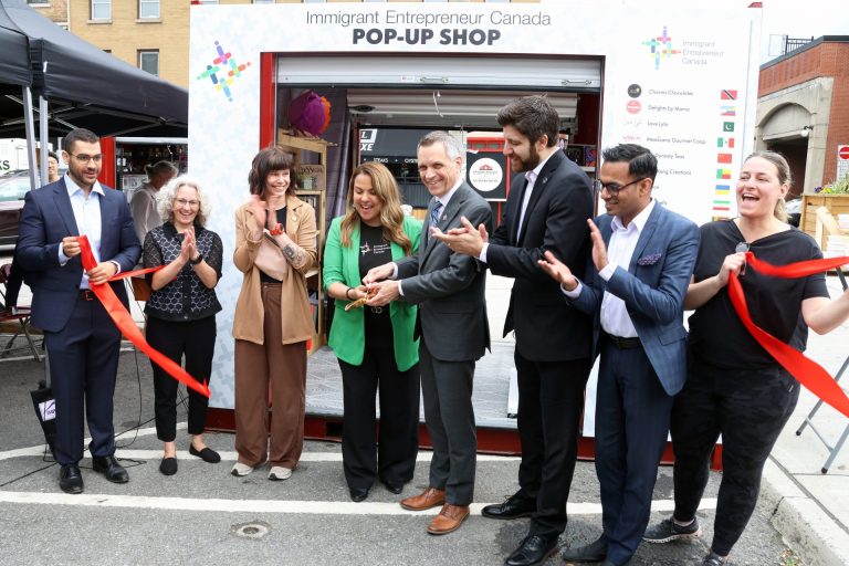From left, Yasser Ghazi (Meridian), Paula Hopkins (Invest Ottawa), Anastasia Temborska (owner of PINBOX), Immigrant Entrepreneur Canada founder and CEO Karla Briones, Ottawa Mayor Mark Sutcliffe, Syrian-Canadian entrepreneur Tareq Hadhad (Peace by Chocolate), Daniel Thiruganaratnapathy (RBC) and Ottawa city councillor Stéphanie Plante (Rideau-Vanier) at the ribbon-cutting ceremony for IEC's Summer Retail Incubator 2024 program, which includes a pop-up shop in the ByWard Market. Photo by Caroline Phillips