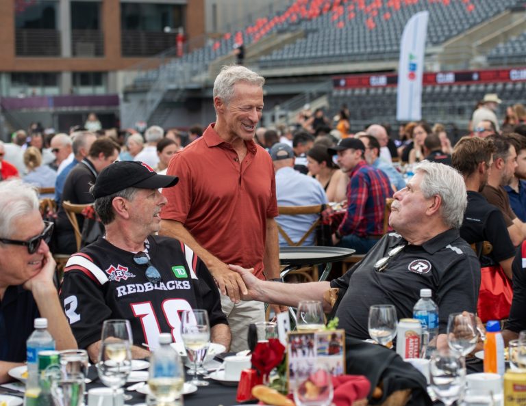 Roger Greenberg, OSEG executive chairman and managing partner and executive chairman of The Minto Group, with Fred Seller, founding partner of Brazeau Seller Law, shaking the hand of John Pugh, partner with OSEG, at Gourmet on the Gridiron, June 24, 2025. Photo by Tia MacPherson.