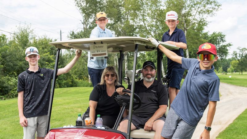 (L-R, standing) Youth Adler Smith, Tommy Davison, Benny Davison, Kennan Ethier have some fun spending the afternoon with Enbridge Team members (sitting) Anik Benoit and Chris Brennan at the Mayor’s Charity Classic in support of Youth Ottawa at The Meadows Golf & Country Club, August 6, 2026. Photo by Tia MacPherson-Abdulla/OBJ.